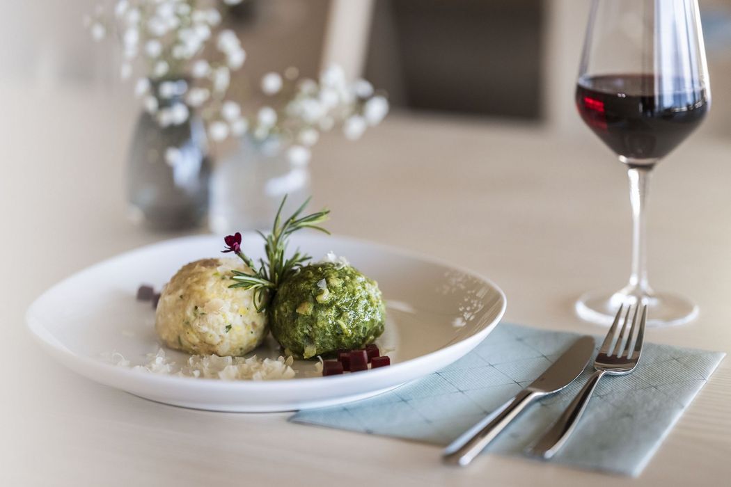 Zwei Knödel auf weißem Teller mit Kräuterzweig, daneben Besteck auf blauer Serviette und ein Glas Rotwein Zwei Knödel auf weißem Teller mit Kräuterzweig, daneben Besteck auf blauer Serviette und ein Glas Rotwein