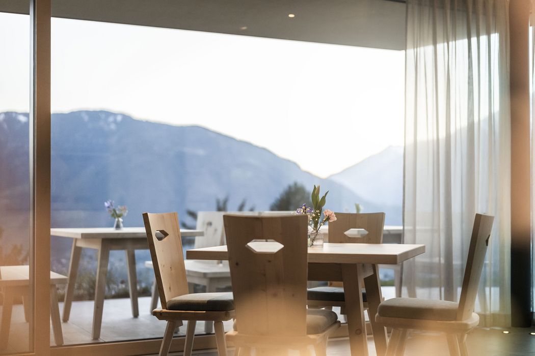 Essbereich mit Holztischen und -stühlen vor großen Fenstern mit Bergblick, Tisch mit kleiner Blumendekoration Essbereich mit Holztischen und -stühlen vor großen Fenstern mit Bergblick, Tisch mit kleiner Blumendekoration