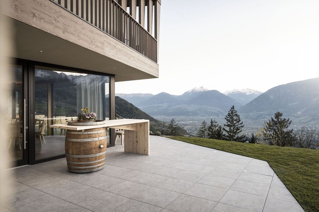 Terrasse mit Tisch aus Holzfass vor modernem Haus mit Bergpanorama im Hintergrund Terrasse mit Tisch aus Holzfass vor modernem Haus mit Bergpanorama im Hintergrund