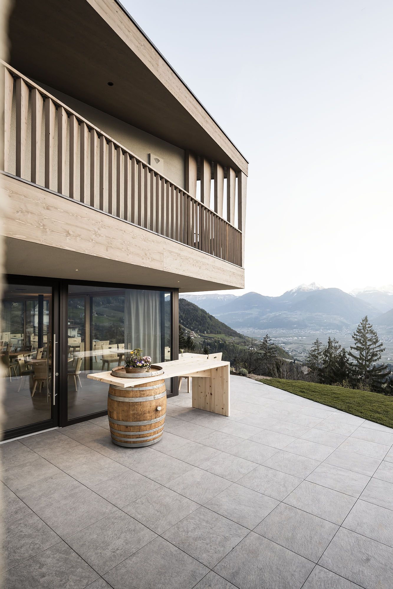 Moderner Holzbau mit Balkon, Terrasse mit Fass und Holztisch, Blick auf Berge und Tal Moderner Holzbau mit Balkon, Terrasse mit Fass und Holztisch, Blick auf Berge und Tal