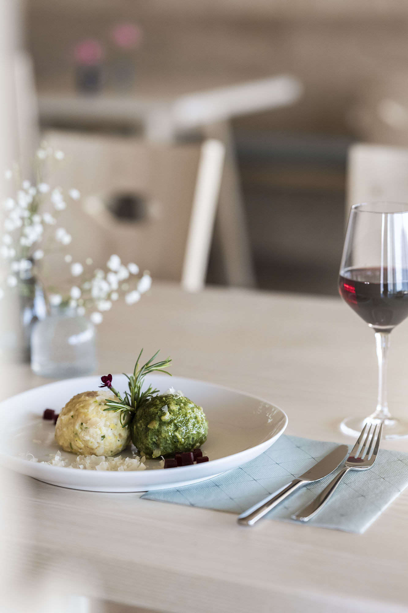 Teller mit zwei Knödeln, ein Glas Rotwein, Besteck auf einem hellen Holztisch Teller mit zwei Knödeln, ein Glas Rotwein, Besteck auf einem hellen Holztisch